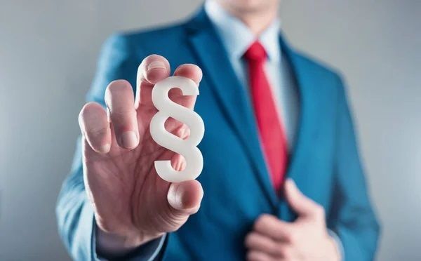 Mężczyzna w garniturze trzymający w dłoni znak paragrafu